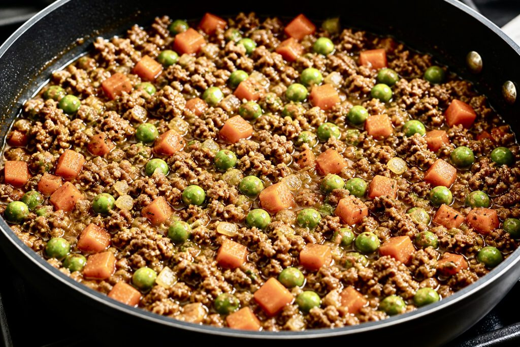 Ground beef with carrots and peas cooking in a pan for cottage pie