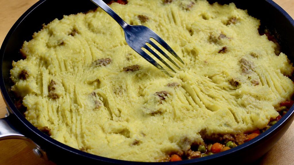 One-pan cottage pie with mashed potatoes being textured with a fork